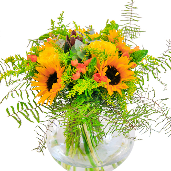 Radiating with warmth, this abundant bouquet is a striking reflection of Harrow on the Hill's vibrant character. Central sunflowers, each a burst of golden brilliance, are framed by lush yellow roses, their ruffled petals forming perfect spirals reminiscent of blooms flourishing in the gardens near Headstone Manor. Here and there, shining clusters of red Hypericum berries provide a joyful contrast, their smooth skins catching the light as they nestle amid a cascade of rich green foliage. The arrangement's greenery sweeps outward: feathery, arching fern fronds and delicate trails of eucalyptus add playful texture, echoing the wild beauty found in Roxeth recreation grounds and tree-lined avenues. The bouquet is presented in a crystal-clear, round glass vase, allowing stems to be seen beneath the water-adding an element of simple elegance and freshness. Every flower and leaf has been thoughtfully selected, conveying not just visual splendour but also the tactile pleasure of velvety petals and crisp, cool greens. There's a subtle, invigorating fragrance: a hint of open fields and sunlit afternoons that linger in the air. This expertly crafted arrangement is the perfect expression of joy and togetherness, an ideal gift for marking special occasions, sending thanks, or delivering a heartfelt gesture to loved ones across Harrow on the Hill. Crafted with an eye for local beauty, it's a celebration of both the season's richest colours and the community's sense of connection.
